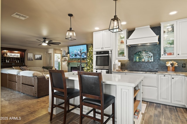 kitchen featuring premium range hood, a breakfast bar area, glass insert cabinets, and white cabinetry