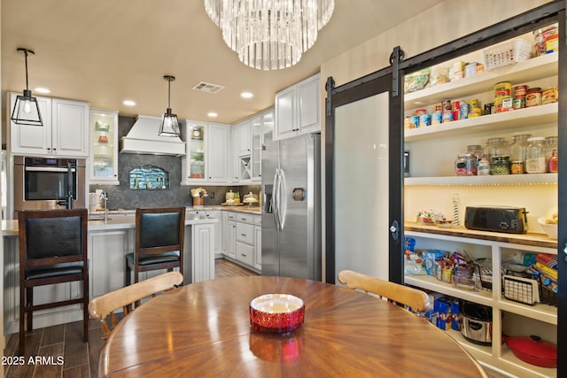 kitchen featuring premium range hood, stainless steel appliances, hanging light fixtures, and glass insert cabinets