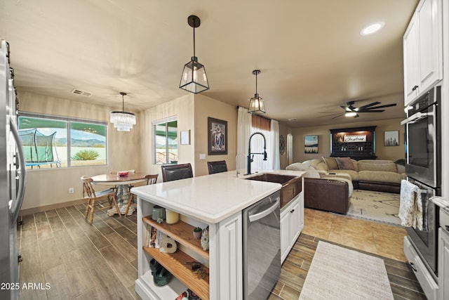 kitchen featuring appliances with stainless steel finishes, hanging light fixtures, a kitchen island with sink, white cabinetry, and a sink