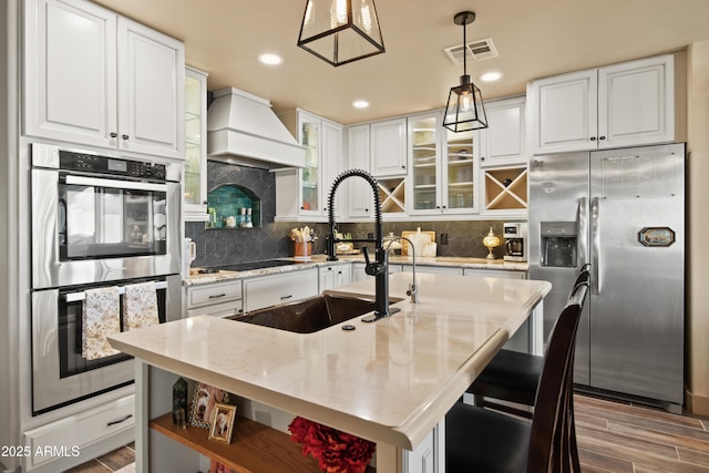 kitchen with decorative light fixtures, open shelves, custom range hood, appliances with stainless steel finishes, and glass insert cabinets