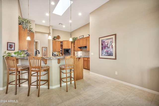 kitchen featuring light stone counters, a breakfast bar, kitchen peninsula, black microwave, and a skylight