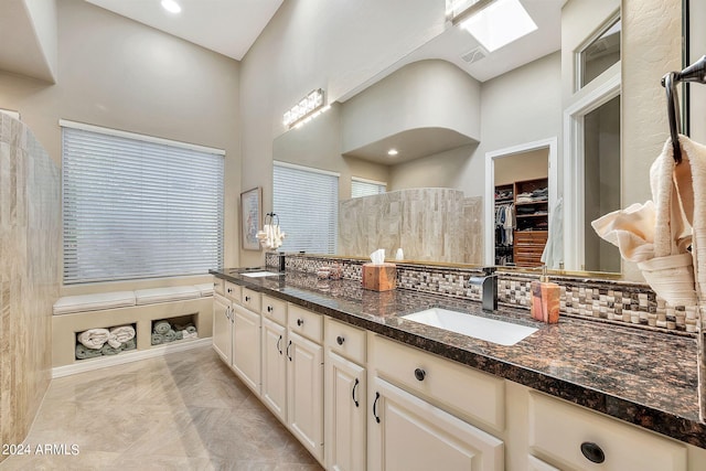 bathroom with a towering ceiling, backsplash, a skylight, and vanity