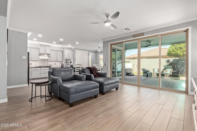 living area with light wood-type flooring, visible vents, ornamental molding, baseboards, and ceiling fan