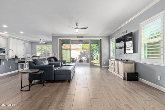 living room featuring crown molding, light wood-style floors, baseboards, and ceiling fan