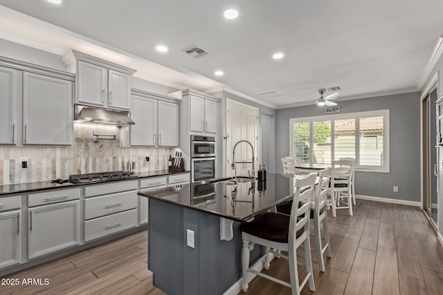 kitchen featuring visible vents, under cabinet range hood, a sink, appliances with stainless steel finishes, and crown molding