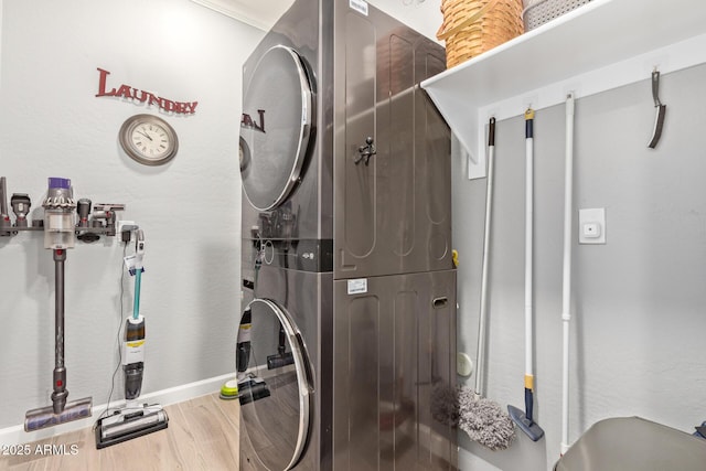 laundry area with baseboards, wood finished floors, laundry area, and stacked washing maching and dryer