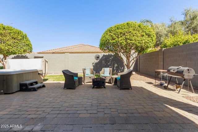 view of patio with grilling area, a hot tub, a fenced backyard, and an outdoor fire pit