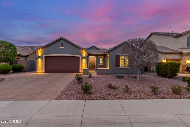 view of front facade featuring fence, a tiled roof, stucco siding, decorative driveway, and a garage