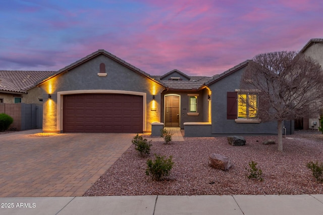 ranch-style house featuring fence, a tiled roof, stucco siding, decorative driveway, and an attached garage