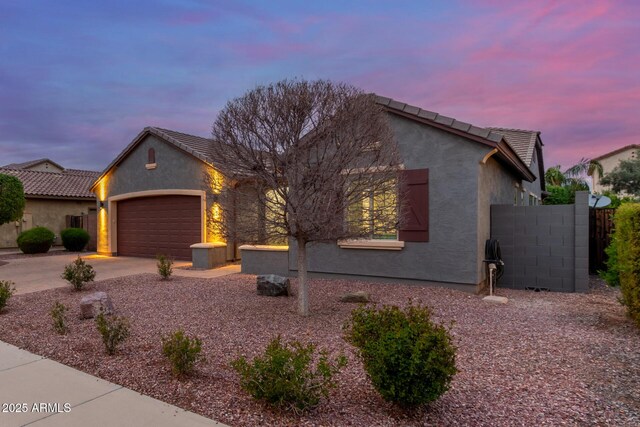 view of front facade with stucco siding, driveway, fence, an attached garage, and a tiled roof