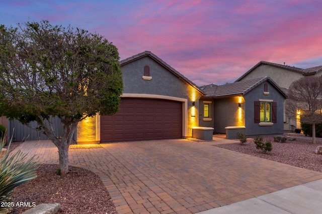 view of front facade with decorative driveway, a tiled roof, an attached garage, and stucco siding