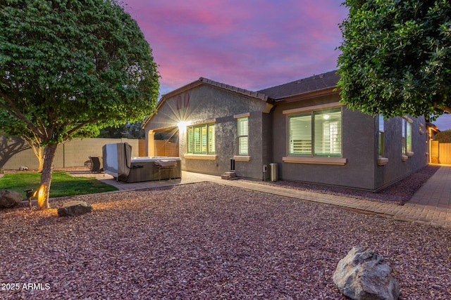 property exterior at dusk featuring a patio, stucco siding, a fenced backyard, and a hot tub