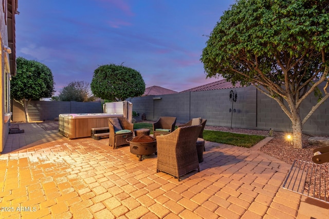 patio terrace at dusk featuring an outdoor fire pit, a fenced backyard, and a hot tub