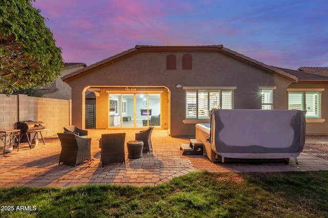 back of property at dusk featuring fence, an outdoor living space, a hot tub, stucco siding, and a patio area