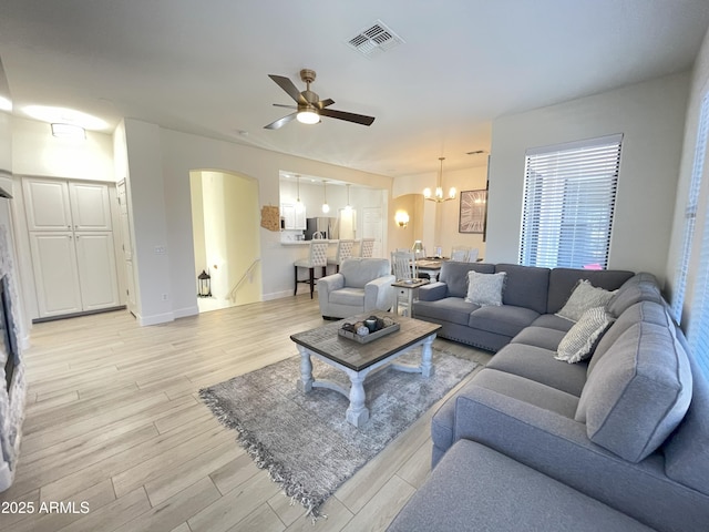 living area with baseboards, visible vents, arched walkways, light wood-type flooring, and ceiling fan with notable chandelier