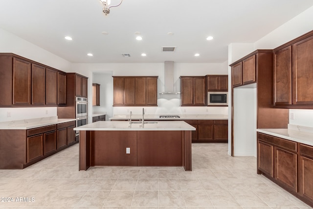 kitchen with light tile patterned flooring, stainless steel appliances, sink, wall chimney exhaust hood, and a kitchen island with sink