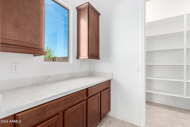 8628 W Solano Dr, Glendale, AZ 85305 - kitchen featuring light stone countertops, brown cabinetry, light tile patterned flooring, and baseboards