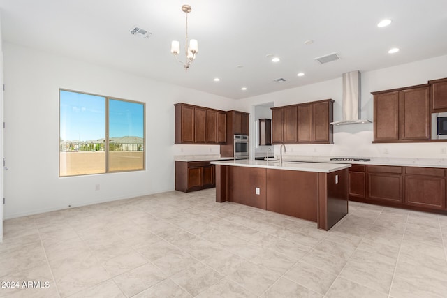 kitchen with a center island with sink, stainless steel appliances, wall chimney range hood, pendant lighting, and a chandelier