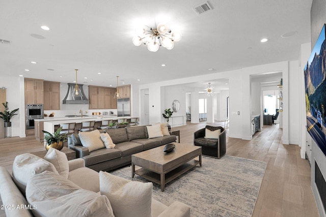 living room with sink, a notable chandelier, and light wood-type flooring