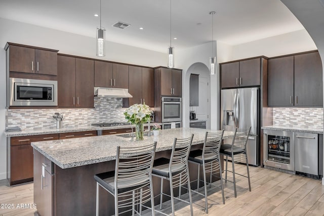 10886 N 137th St, Scottsdale, AZ 85259 - kitchen with visible vents, beverage cooler, under cabinet range hood, arched walkways, and appliances with stainless steel finishes
