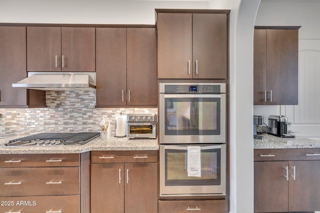 10886 N 137th St, Scottsdale, AZ 85259 - kitchen featuring light stone counters, arched walkways, stainless steel appliances, under cabinet range hood, and backsplash