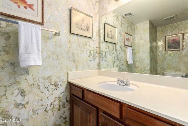 bathroom featuring visible vents, vanity, and wallpapered walls