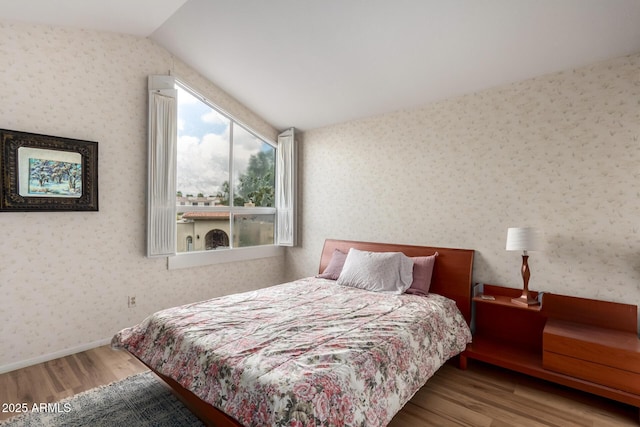 bedroom with baseboards, wood finished floors, vaulted ceiling, and wallpapered walls