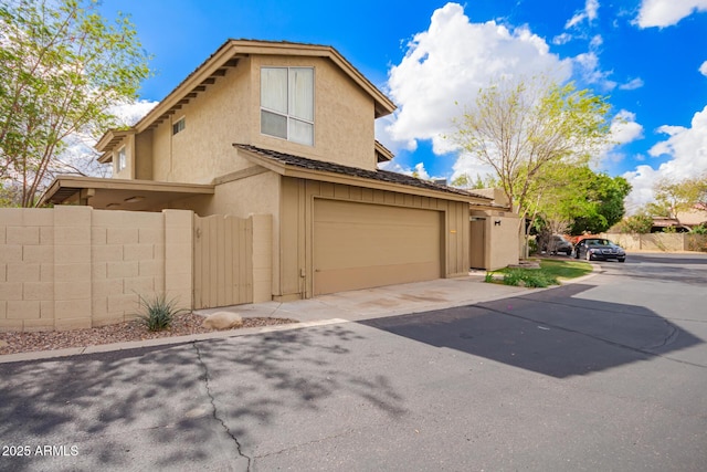 view of side of property featuring stucco siding, a garage, driveway, and fence