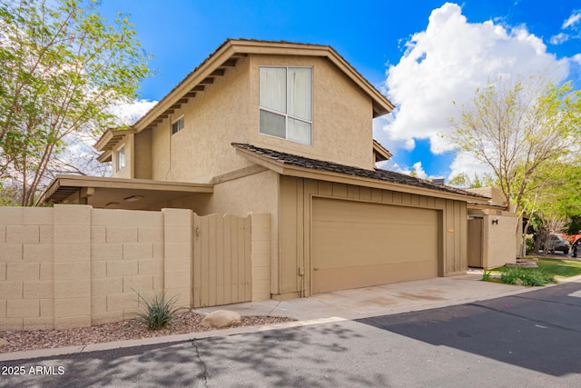 view of front of home featuring stucco siding, driveway, a gate, fence, and an attached garage