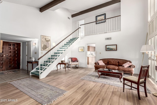 living area with visible vents, beam ceiling, wood finished floors, a high ceiling, and stairs