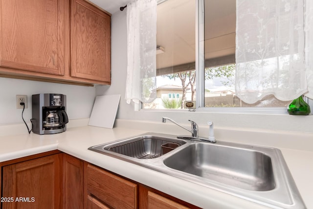 kitchen with brown cabinetry, light countertops, and a sink