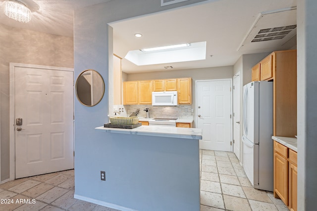 kitchen with white appliances, a skylight, light brown cabinetry, tasteful backsplash, and kitchen peninsula