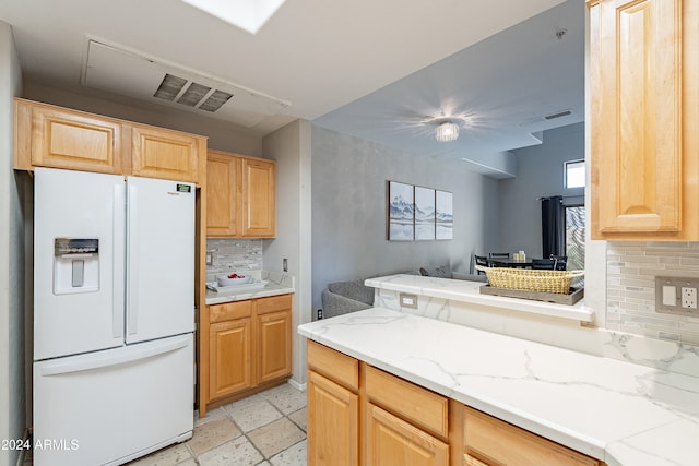 kitchen featuring white refrigerator with ice dispenser, light brown cabinets, and backsplash