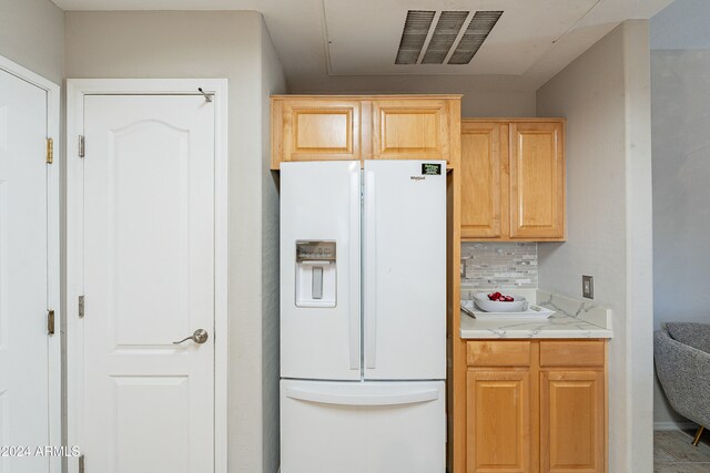 kitchen with decorative backsplash, light brown cabinetry, and white fridge with ice dispenser