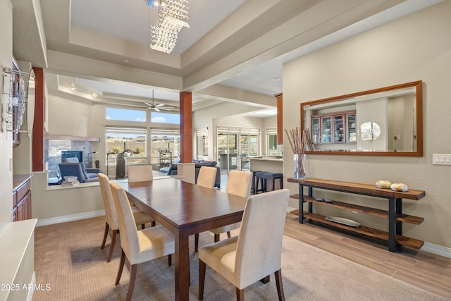 dining space featuring light hardwood / wood-style floors, ceiling fan with notable chandelier, a fireplace, and a tray ceiling