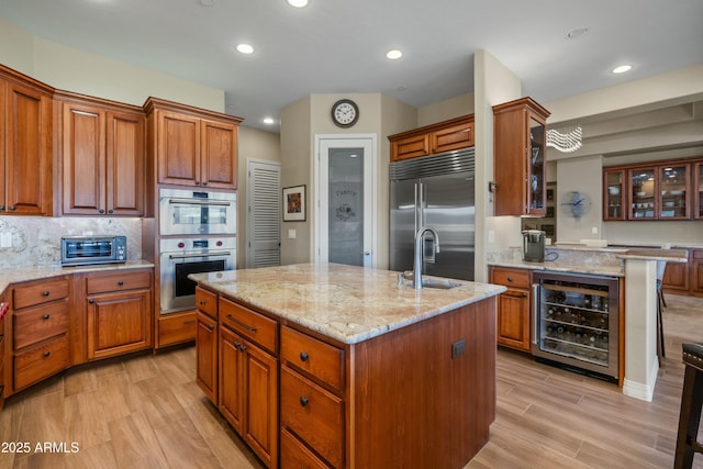 kitchen featuring sink, tasteful backsplash, beverage cooler, a center island with sink, and appliances with stainless steel finishes