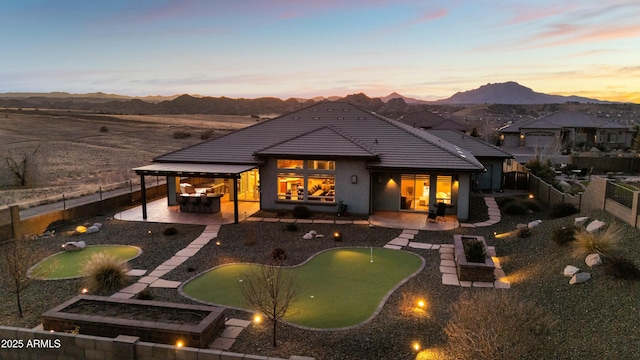 back house at dusk featuring a mountain view and a patio area