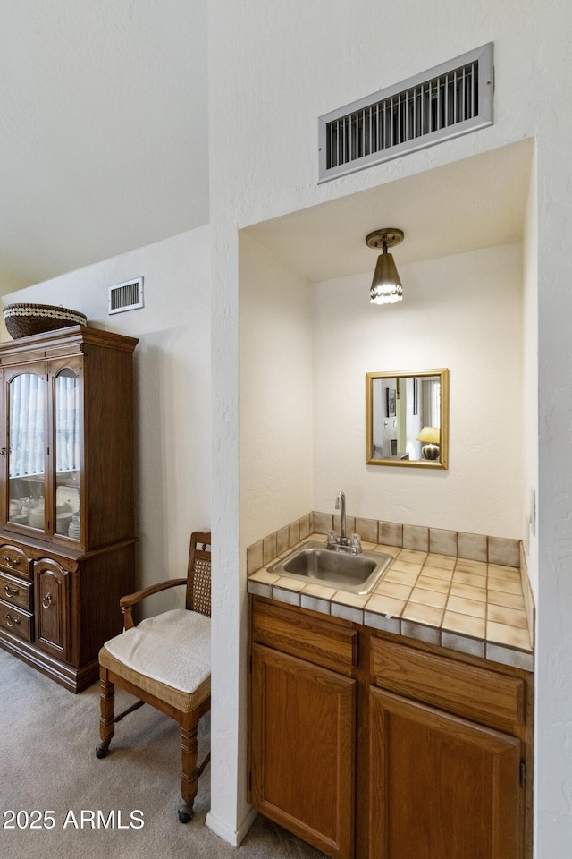 kitchen featuring carpet floors, tile countertops, visible vents, and a sink