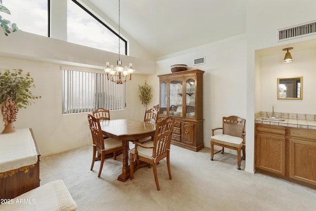 dining area with light carpet, high vaulted ceiling, visible vents, and an inviting chandelier