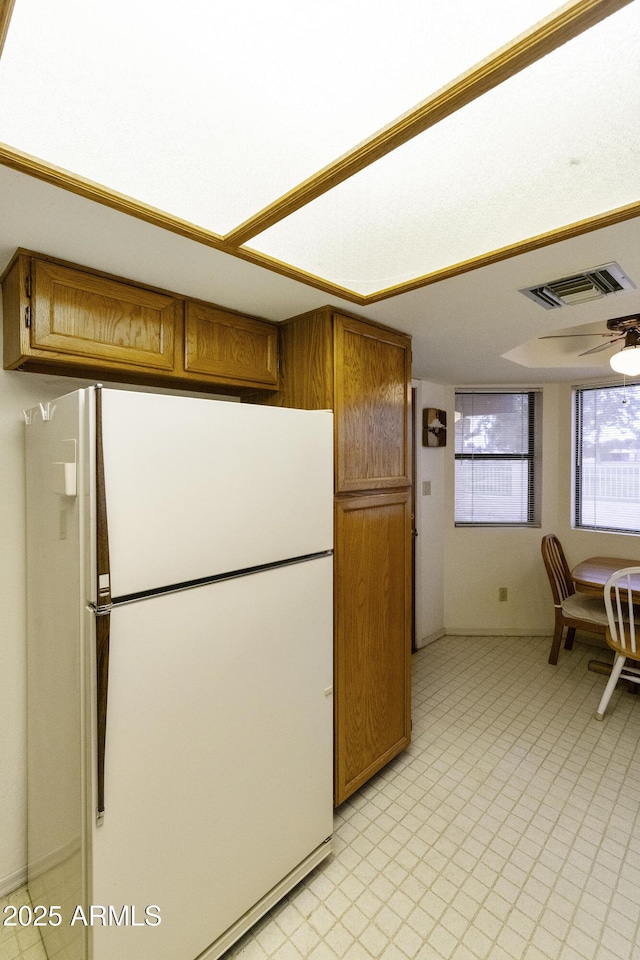 kitchen featuring brown cabinets, freestanding refrigerator, visible vents, and light floors