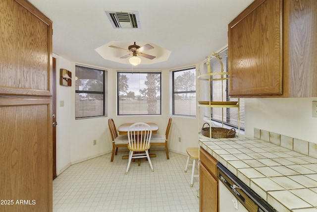 interior space with ceiling fan, visible vents, baseboards, tile counters, and a tray ceiling