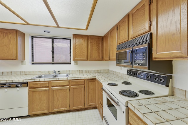 kitchen with tile counters, white appliances, brown cabinetry, and a sink