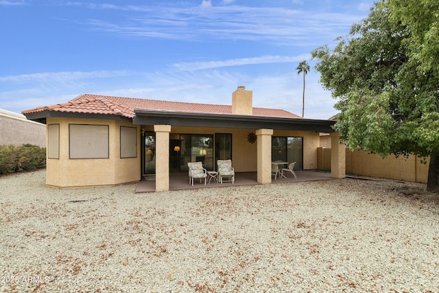 back of house with fence, a tiled roof, stucco siding, a chimney, and a patio area