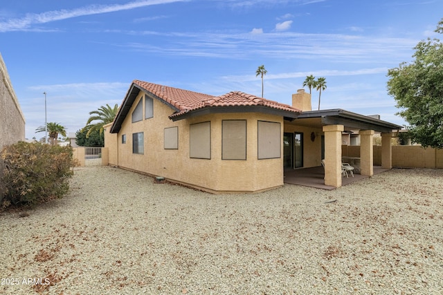 rear view of house with a patio, a chimney, a tiled roof, fence, and stucco siding