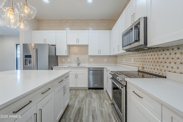 kitchen with white cabinetry, stainless steel appliances, sink, and hanging light fixtures