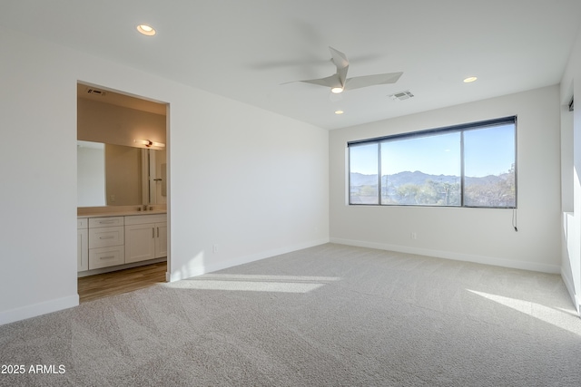 unfurnished bedroom featuring sink, light colored carpet, ceiling fan, a mountain view, and ensuite bath