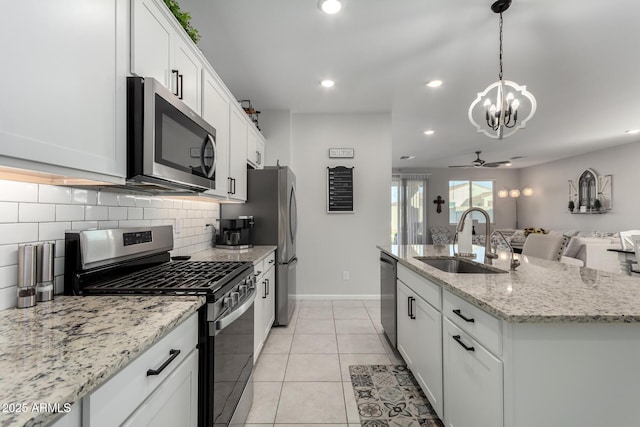 kitchen with ceiling fan with notable chandelier, white cabinetry, stainless steel appliances, sink, and a center island with sink