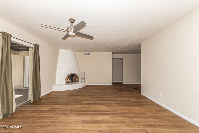 unfurnished living room with ceiling fan, wood-type flooring, a large fireplace, and a textured ceiling