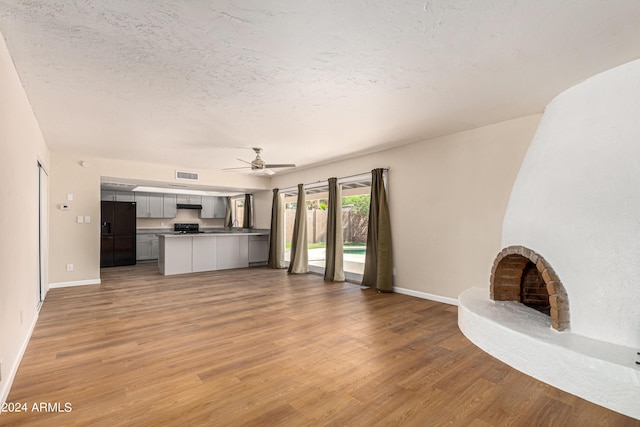 unfurnished living room with ceiling fan, light wood-type flooring, a textured ceiling, and a fireplace