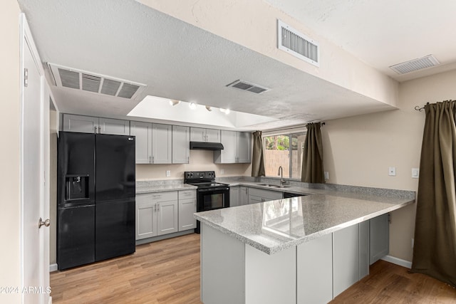 kitchen with light hardwood / wood-style floors, gray cabinets, black appliances, and kitchen peninsula